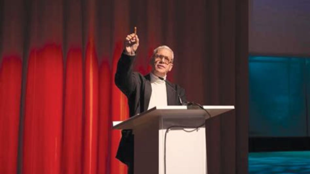 Prof. Mooli Lahad standing at a podium and pointing out to the crowd in front of a red curtain
